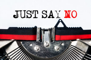 A close-up of the type-wheel and ribbon of an old typewriter with the words "Just say no," in all caps. The "no" is in red.